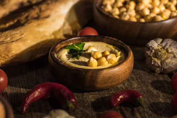 Foco seletivo de delicioso hummus, grão de bico, pita, legumes e especiarias na mesa rústica de madeira — Fotografia de Stock