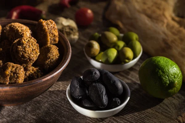 Selective focus of delicious falafel balls near lime, black and green olives on wooden rustic table — Stock Photo