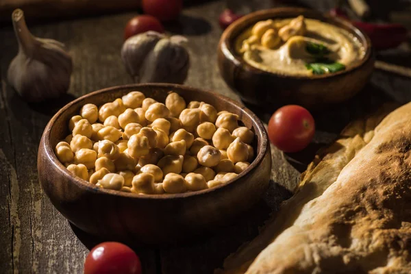 Foco seletivo de delicioso hummus, grão de bico, pita, legumes e especiarias na mesa rústica de madeira — Fotografia de Stock