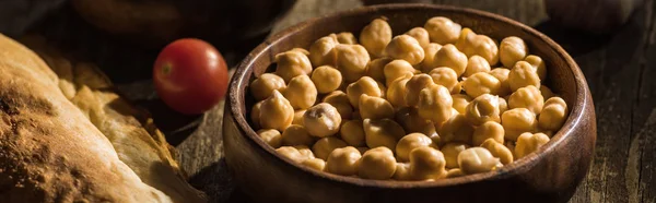 Deliciosos garbanzos, pita, tomate cherry sobre mesa rústica de madera, plano panorámico - foto de stock