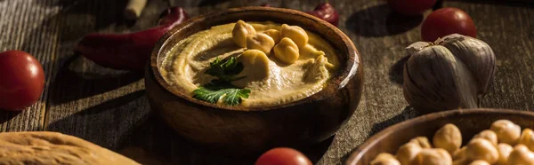 Köstlicher Hummus, Kichererbsen, Pita, Gemüse und Gewürze auf rustikalem Holztisch, Panoramaaufnahme — Stockfoto