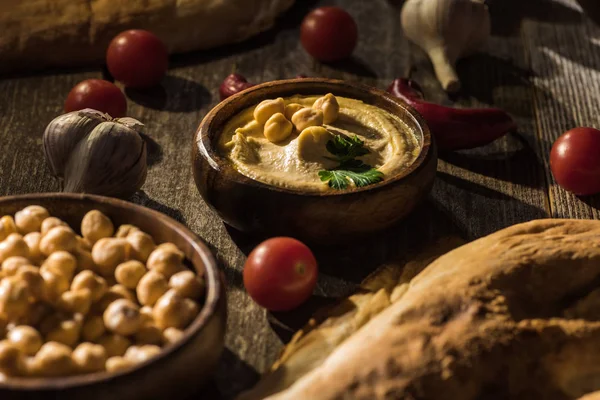 Delicious hummus, chickpeas, pita, vegetables and spices on wooden rustic table — Stock Photo