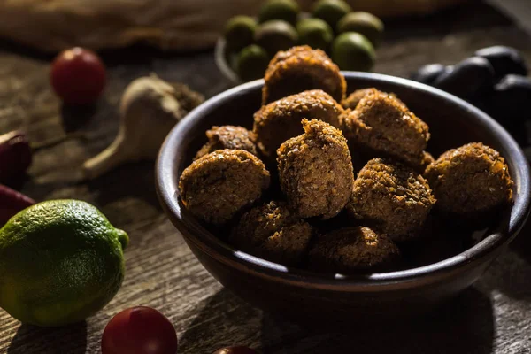 Foco seletivo de deliciosas bolas de falafel perto de limão, azeitonas pretas e verdes em mesa rústica de madeira — Fotografia de Stock