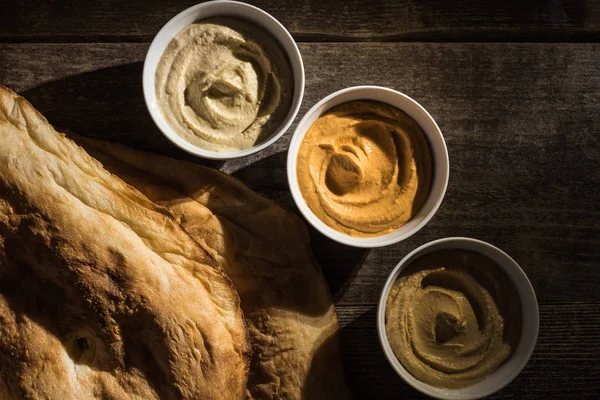 Vue de dessus de délicieux houmous assortis près de pita fraîche cuite au four sur table rustique en bois — Photo de stock