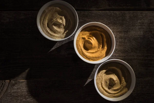 Draufsicht auf köstlich sortierten Hummus auf rustikalem Holztisch — Stockfoto