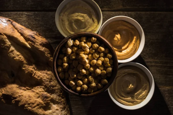 Вид на вкусный разнообразный хумус, горох и свежую запеченную питу на деревянном деревенском столе — стоковое фото