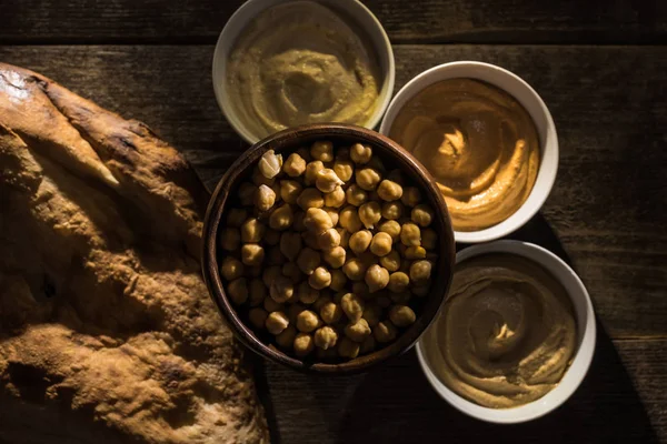 Vue de dessus de délicieux houmous assortis, pois chiches et pita fraîche cuite au four sur table rustique en bois — Photo de stock