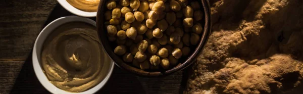 Vista superior do hummus sortido delicioso, grão de bico e pita cozido fresco na mesa rústica de madeira, tiro panorâmico — Fotografia de Stock