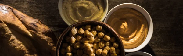 Vue de dessus de délicieux houmous assortis, pois chiches et pita fraîche cuite au four sur une table rustique en bois, vue panoramique — Photo de stock