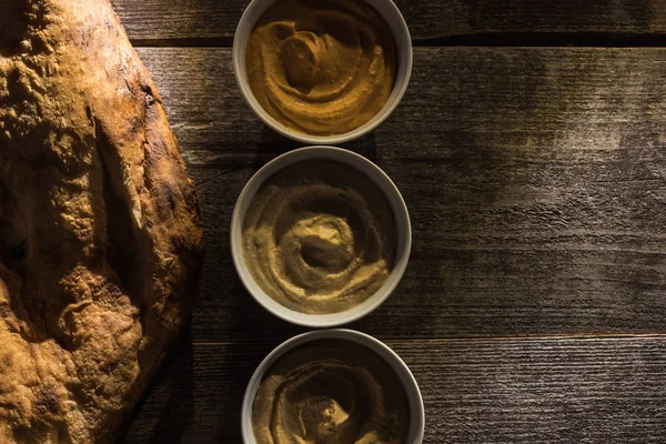 Vista dall'alto di deliziosi hummus assortiti e pita appena sfornata su tavolo rustico in legno — Foto stock