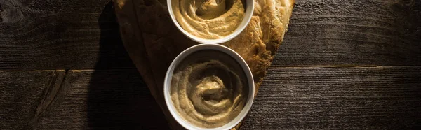 Draufsicht auf köstlich sortierten Hummus auf frisch gebackenem Fladenbrot auf rustikalem Holztisch, Panoramaaufnahme — Stockfoto