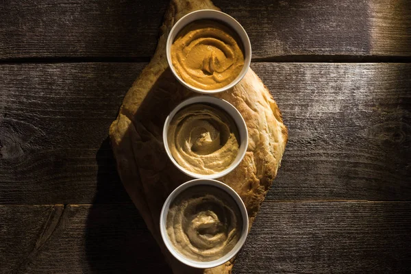 Vue de dessus de délicieux houmous assortis sur pita fraîche cuite au four sur table rustique en bois — Photo de stock