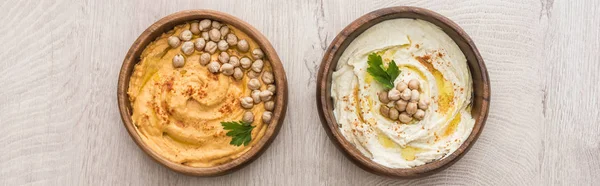 Vista superior de delicioso hummus com grão de bico em tigelas em mesa de madeira bege, tiro panorâmico — Fotografia de Stock