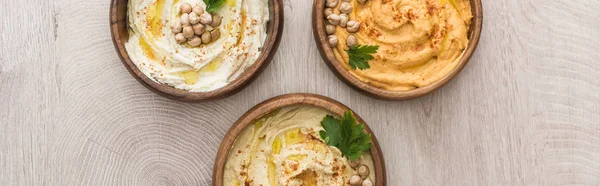 Vista superior de delicioso hummus com grão de bico em tigelas em mesa de madeira bege, tiro panorâmico — Fotografia de Stock