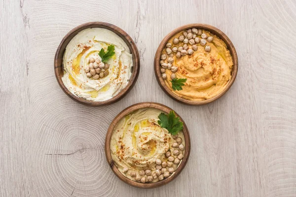 Draufsicht auf köstlichen Hummus mit Kichererbsen in Schalen auf beigem Holztisch — Stockfoto