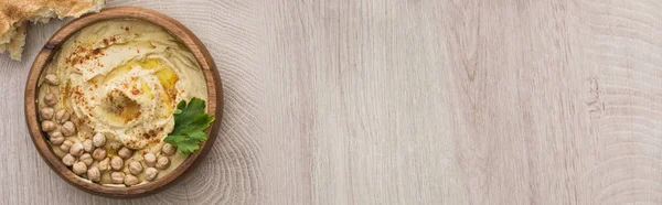 Vue du dessus de délicieux houmous aux pois chiches dans un bol près d'une pita fraîche cuite au four sur une table en bois beige, panoramique — Photo de stock