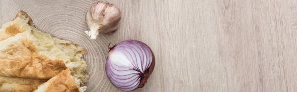 Blick von oben auf köstliche frisch gebackene Pita, Knoblauch und rote Zwiebel auf beigem Holztisch, Panoramaaufnahme — Stockfoto