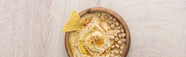 Vue du dessus de délicieux houmous aux pois chiches et nacho dans un bol sur table en bois beige, panoramique — Photo de stock