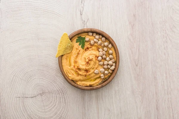 Top view of delicious hummus with chickpeas and nacho in bowl on beige wooden table — Stock Photo