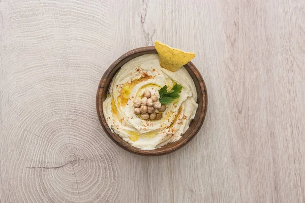 Draufsicht auf köstlichen Hummus mit Kichererbsen und Nacho in Schale auf beigem Holztisch — Stockfoto