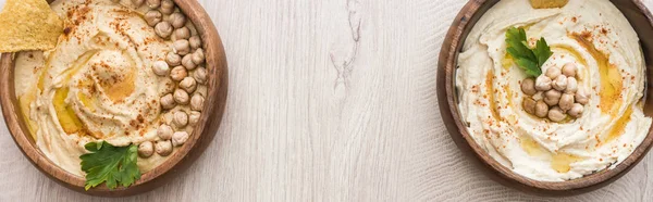 Vue de dessus de délicieux houmous aux pois chiches dans des bols sur table en bois beige, vue panoramique — Photo de stock