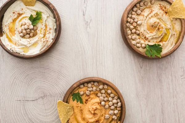 Vista superior de delicioso hummus com grão de bico e nachos em tigelas em mesa de madeira bege — Fotografia de Stock