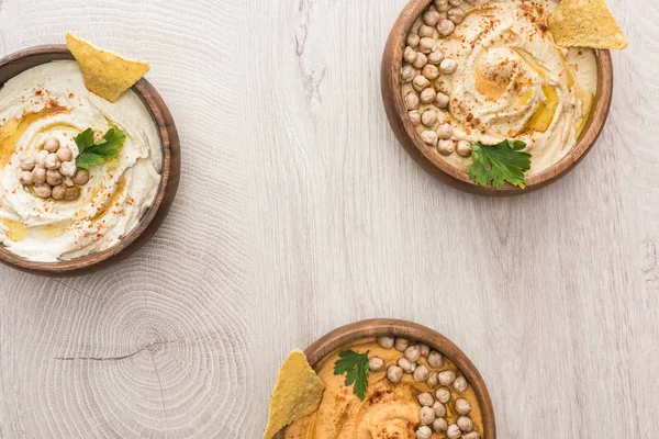 Vista superior de delicioso hummus com grão de bico e nachos em tigelas em mesa de madeira bege — Fotografia de Stock