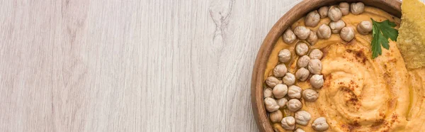 Vue du dessus de délicieux houmous aux pois chiches et nacho dans un bol sur table en bois beige, panoramique — Photo de stock