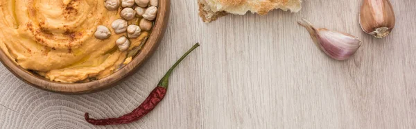 Top view of delicious hummus with chickpeas in bowl near fresh baked pita and spices on beige wooden table, panoramic shot — Stock Photo