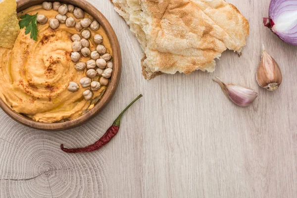 Vista superior do delicioso húmus com grão de bico na tigela perto de pita cozido no forno fresco e especiarias na mesa de madeira bege — Fotografia de Stock