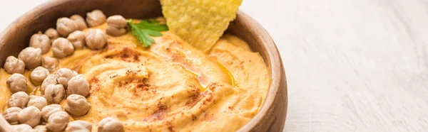 Vista de perto do delicioso hummus com grão de bico e nacho na tigela em mesa de madeira bege, tiro panorâmico — Fotografia de Stock
