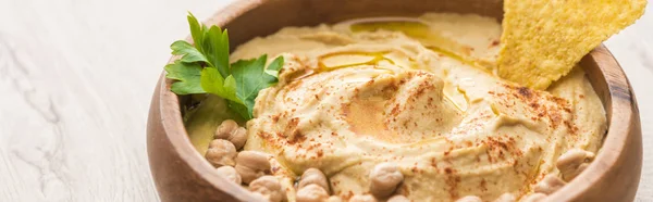 Vue rapprochée de délicieux houmous aux pois chiches et nacho dans un bol sur table en bois beige, vue panoramique — Photo de stock