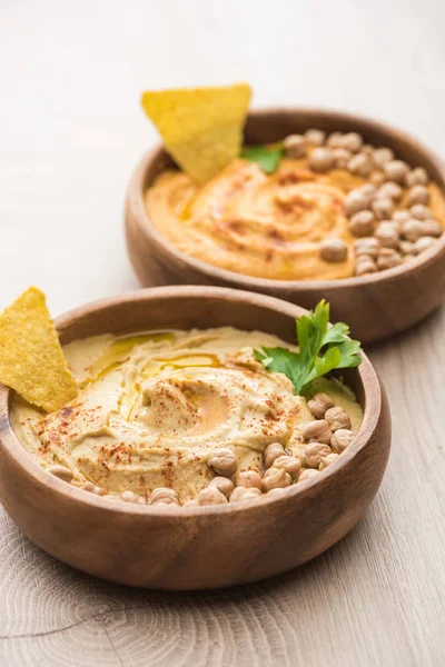 Enfoque selectivo de delicioso hummus con garbanzos y nacho en cuencos sobre mesa de madera beige - foto de stock
