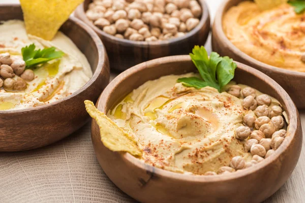 Close up view of delicious hummus with chickpeas and nacho in bowls on beige wooden table — Stock Photo