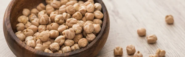 Chickpeas scattered from bowl on beige wooden table, panoramic shot — Stock Photo