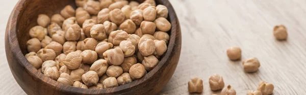 Pois chiches éparpillés dans un bol sur une table en bois beige, vue panoramique — Photo de stock