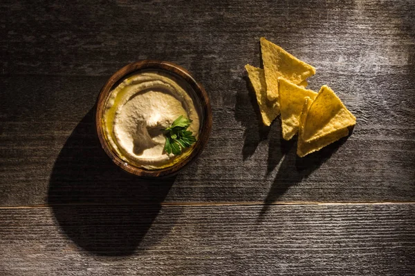 Vue de dessus de délicieux houmous avec des nachos de maïs sur table rustique en bois — Photo de stock