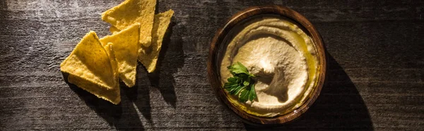 Draufsicht auf köstlichen Hummus mit Mais-Nachos auf rustikalem Holztisch, Panoramaaufnahme — Stockfoto