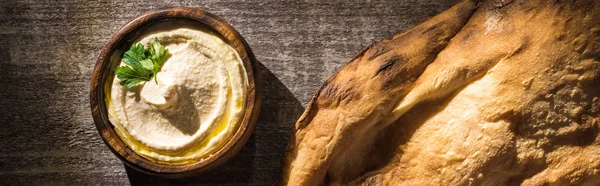 Top view of delicious hummus near fresh baked pita on wooden rustic table, panoramic shot — Stock Photo