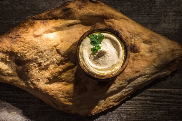Blick von oben auf köstlichen Hummus in der Nähe von frisch gebackener Pita auf rustikalem Holztisch — Stockfoto