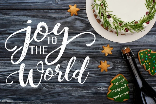 Top view of christmas pie, bottle of champagne and christmas tree cookies on dark wooden table with joy to the world illustration — Stock Photo