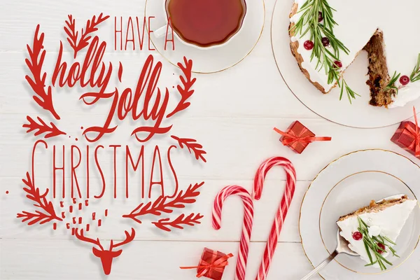 Vue du dessus de tarte de Noël sur table en bois blanc avec tasse de thé, cannes à bonbons et petits cadeaux avec un houx joyeux lettrage de Noël — Photo de stock