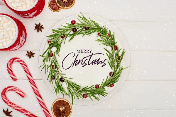 Vista superior de bengalas doces, duas xícaras de cacau e torta de Natal com ilustração Feliz Natal na mesa de madeira branca — Fotografia de Stock