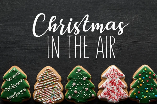 Acostado plano con deliciosas galletas de árbol de Navidad esmaltadas sobre fondo negro con ilustración de Navidad en el aire - foto de stock