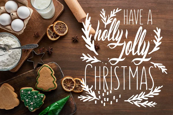 Vue du dessus de délicieux biscuits de Noël près des ingrédients et des épices sur une table en bois avec un lettrage de Noël joyeux houx — Photo de stock