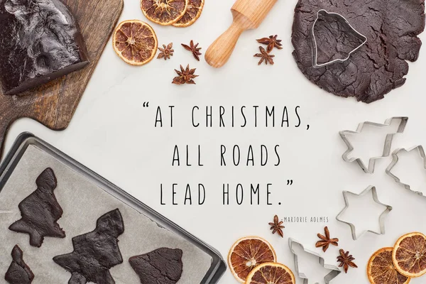 Vue du dessus de la pâte crue pour les biscuits de Noël au chocolat près des ingrédients sur fond blanc avec à Noël toutes les routes mènent à la maison devis — Photo de stock