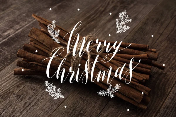 Cinnamon sticks in bunch on wooden rustic table with merry christmas illustration — Stock Photo