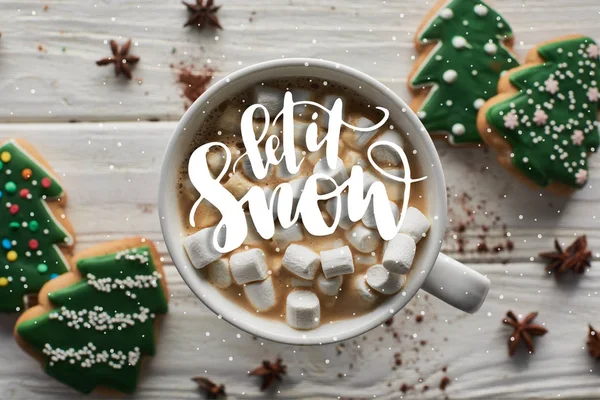 Top view of Christmas cacao with marshmallow in mug on white wooden table near anise and cookies with let it snow illustration — Stock Photo