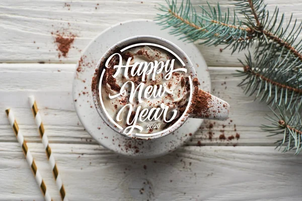 Vista superior de cacao de Navidad con polvo de cacao y crema batida en taza en mesa de madera blanca cerca de rama de abeto con feliz año nuevo letras - foto de stock