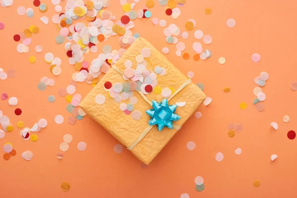 Top view of gift box with blue bow near confetti on orange — Stock Photo